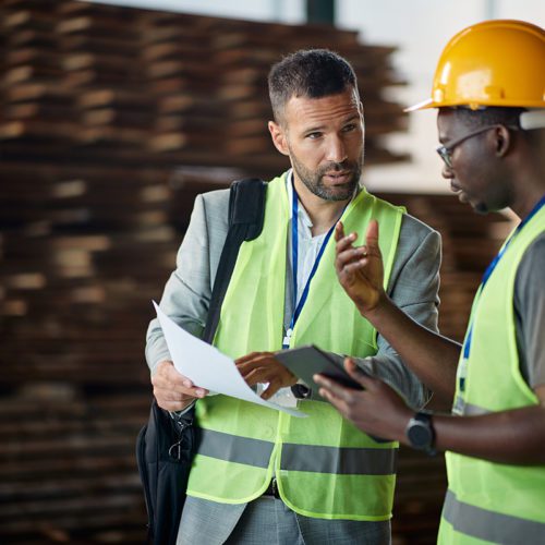 Warehouse manager talking to African American worker while going through reports at wood warehouse.